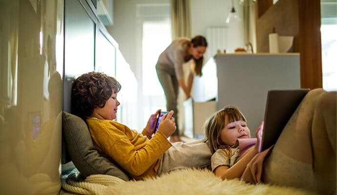 Niños que utilizan tabletas con la madre en segundo plano