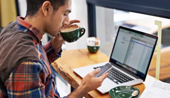 Hombre bebiendo café mientras mira su teléfono.