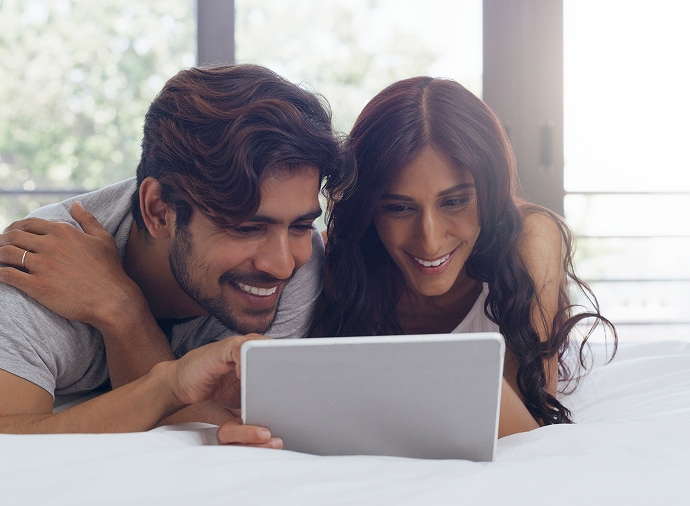 Hombre y mujer riendo mientras observan una tableta